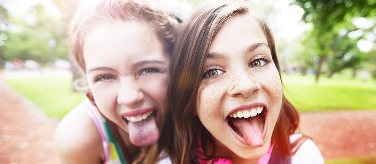 Zwei junge Mädchen, die die Zunge rausstrecken.