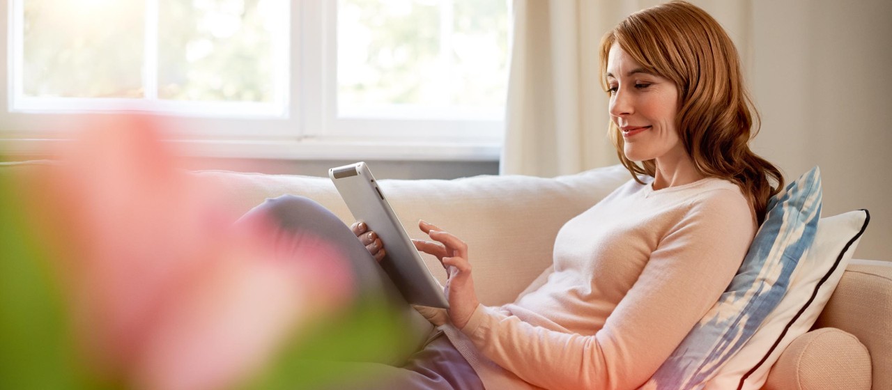 Frau mit Tablet auf dem Sofa surft entspannt im Internet.